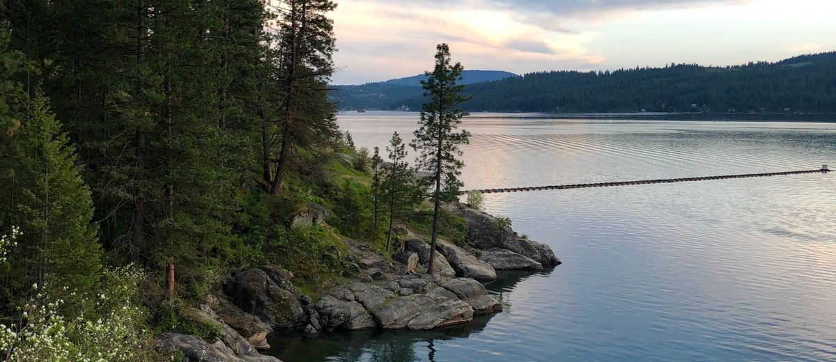 Sunset over Lake Coeur d'Alene with a rocky, pine-lined shoreline in North Idaho